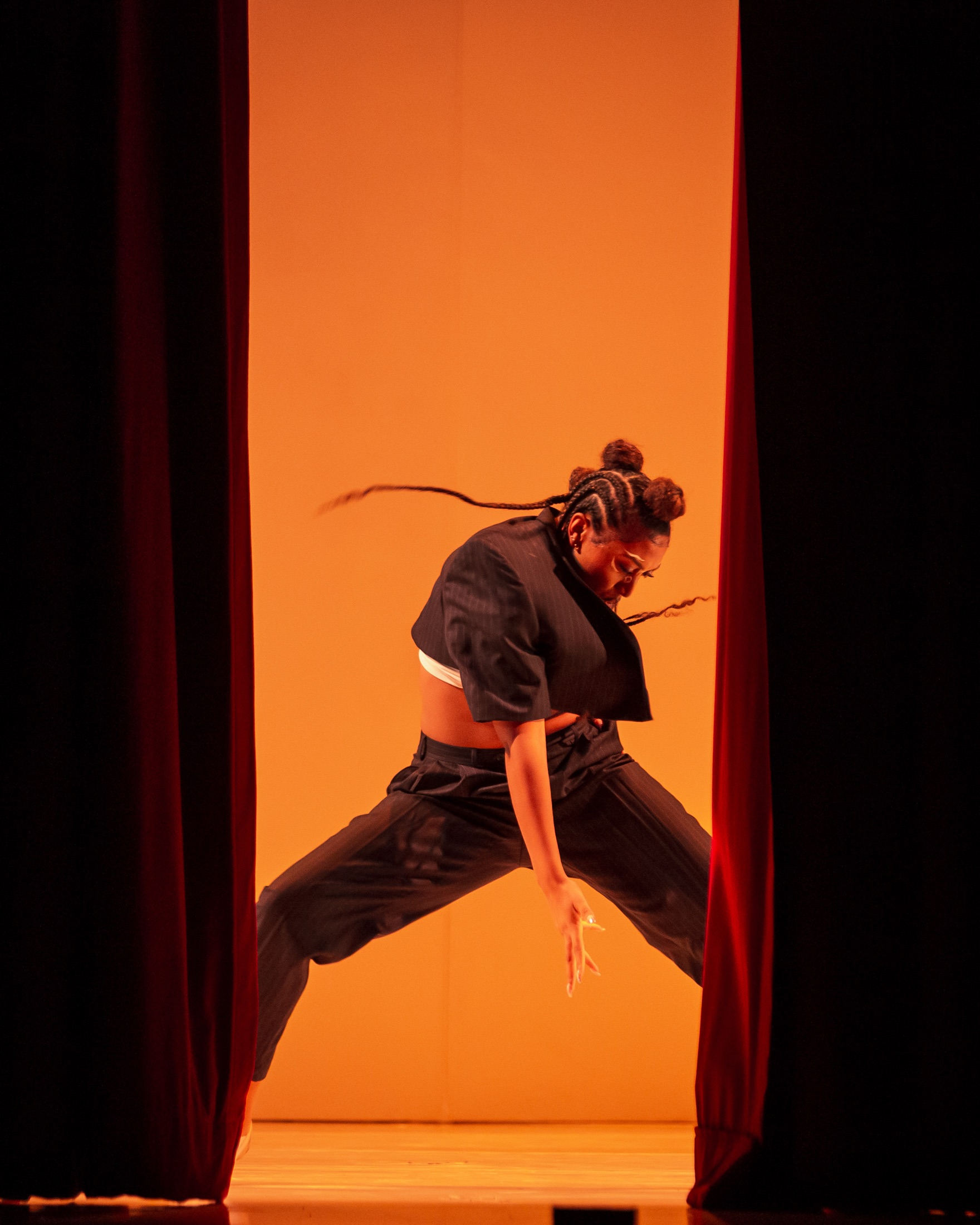 A dancer leaping through red stage curtains lit from behind in orange
