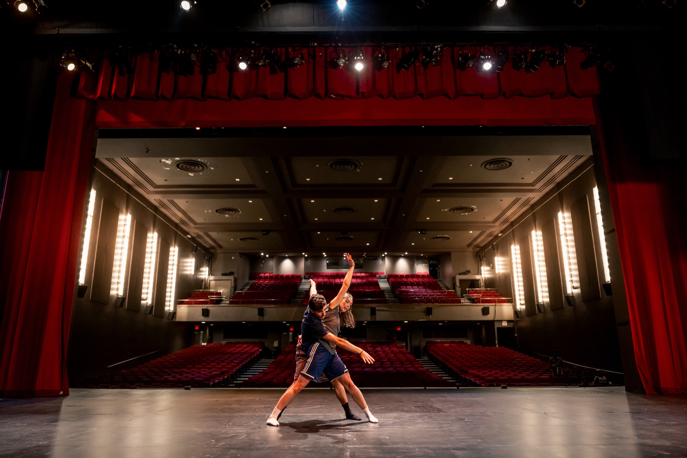 Two dancers in a lifted pose on stage with the empty red-seat house behind them