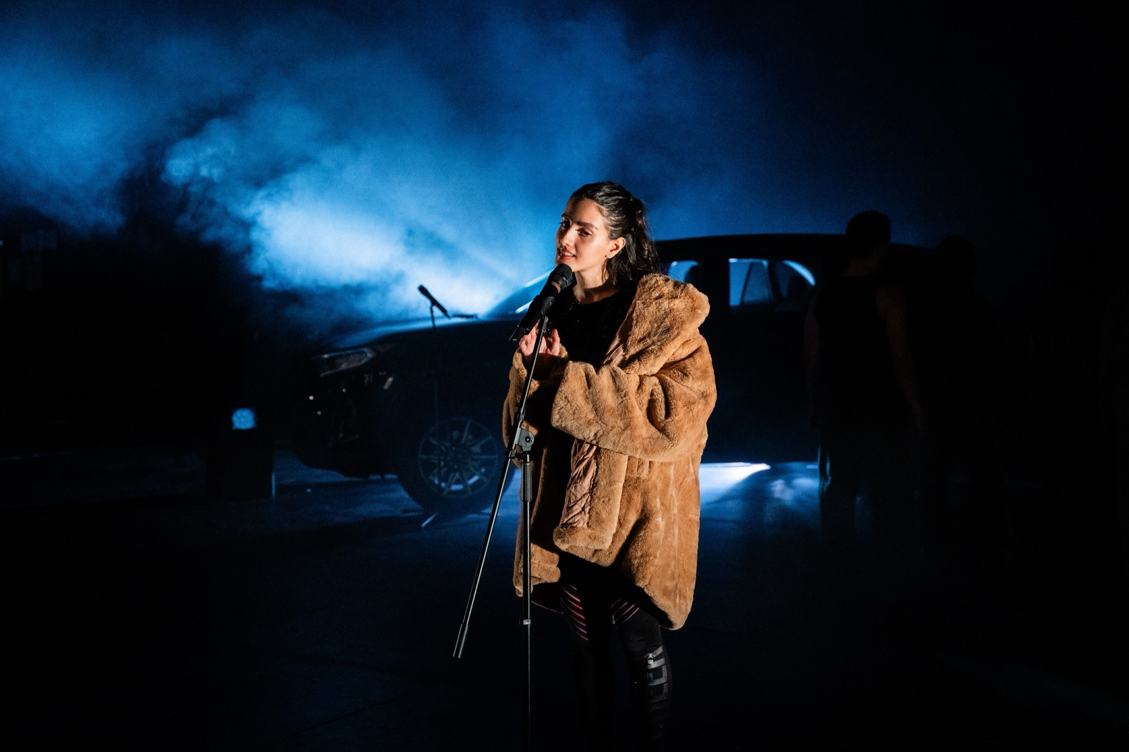 A singer in a fur coat at a microphone stand in a smoky, blue-lit scene