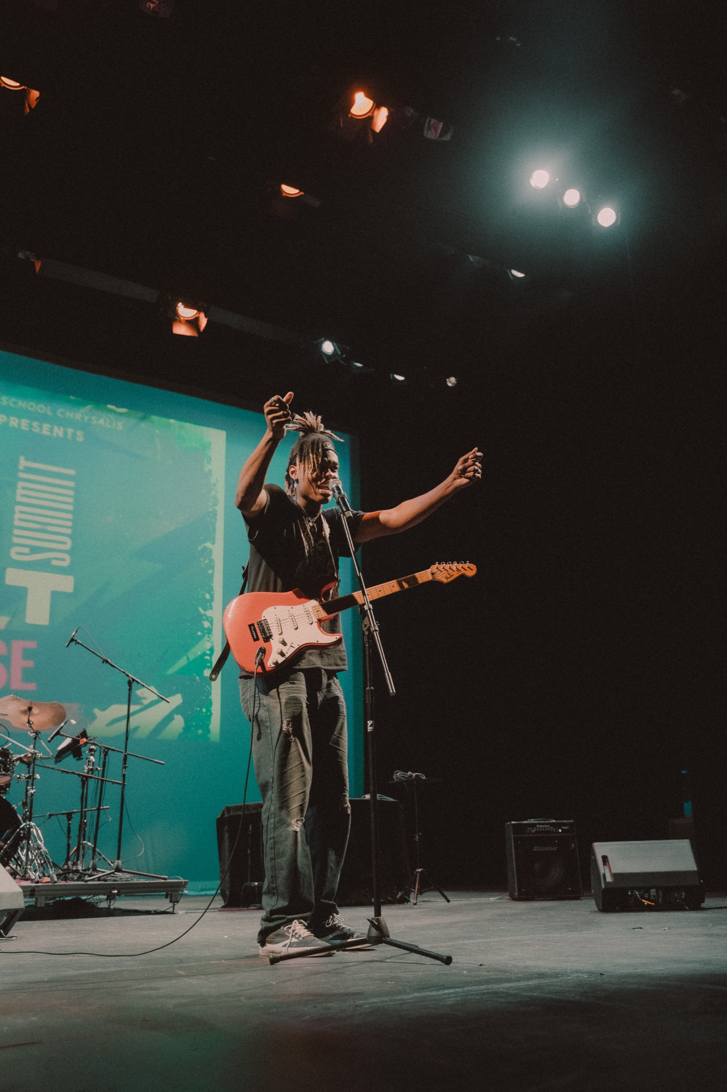 A performer on stage with a guitar in front of a teal branded projection