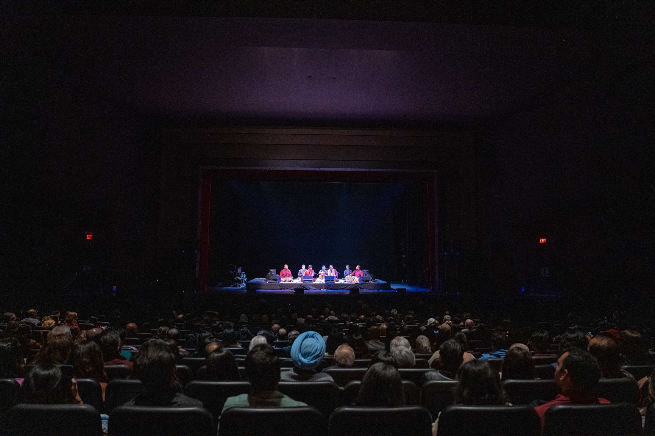 A qawwali ensemble performing on stage with audience silhouettes in the foreground