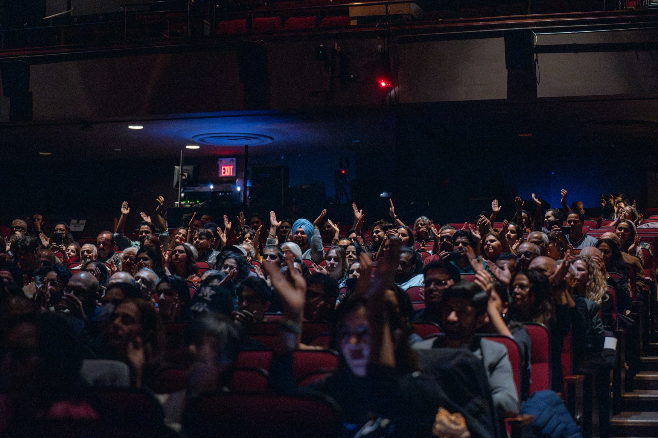 An audience with hands raised, clapping along at a concert